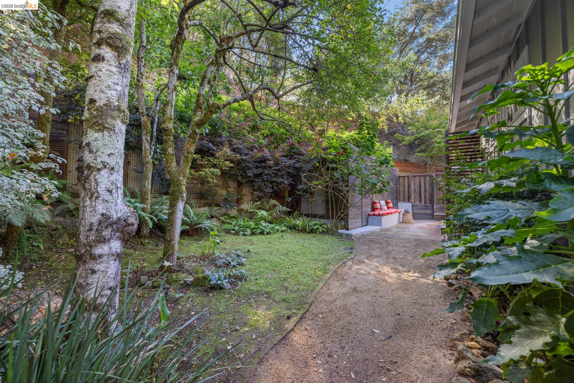 6660 Sobrante Road Oakland, CA 94611 - Photo 37 of 48 Expansive backyard featuring a gravel pathway, mature trees, manicured lawn, and a built-in outdoor seating area