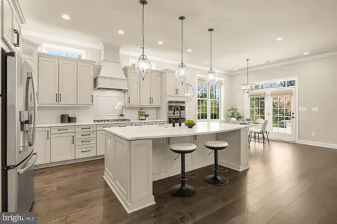 a kitchen with stainless steel appliances kitchen island granite countertop a refrigerator a stove a dining table and chairs with wooden floor