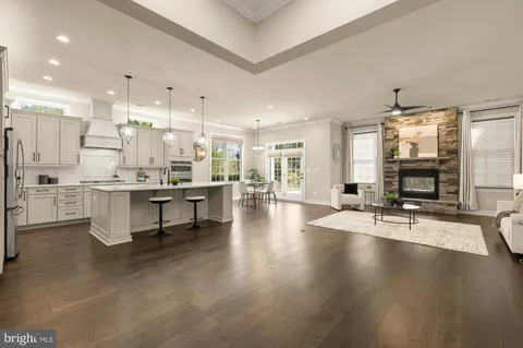 a room with stainless steel appliances kitchen island granite countertop a stove a sink a refrigerator and a dining table with wooden floor