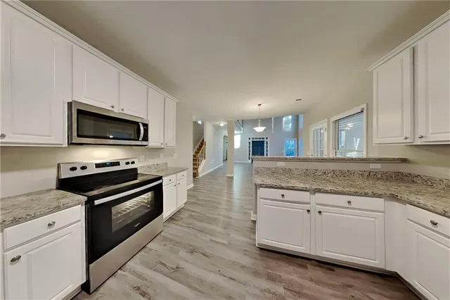 a kitchen with stainless steel appliances granite countertop a stove top oven a sink dishwasher and a microwave oven with wooden floor