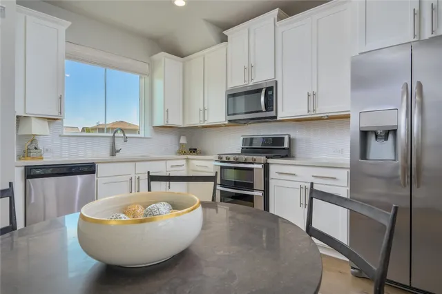 a kitchen with stainless steel appliances granite countertop a stove a sink dishwasher and a refrigerator with white cabinets