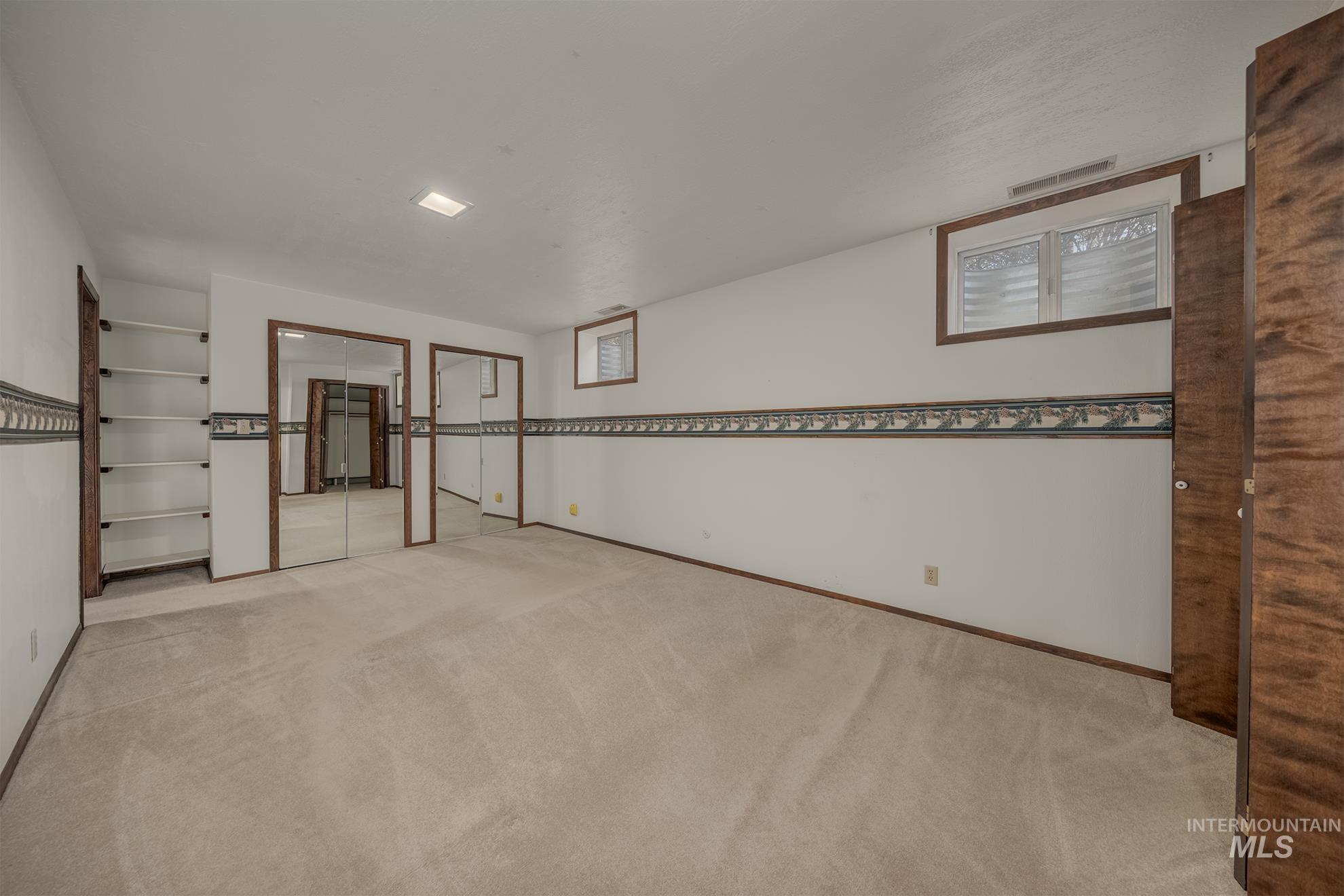 1493 Cove Road Weiser, ID 83672 - Photo 26 of 50 Spacious room featuring neutral carpeting, built-in shelving, two mirrored closet doors, a small window with wood trim, and a patterned wall border