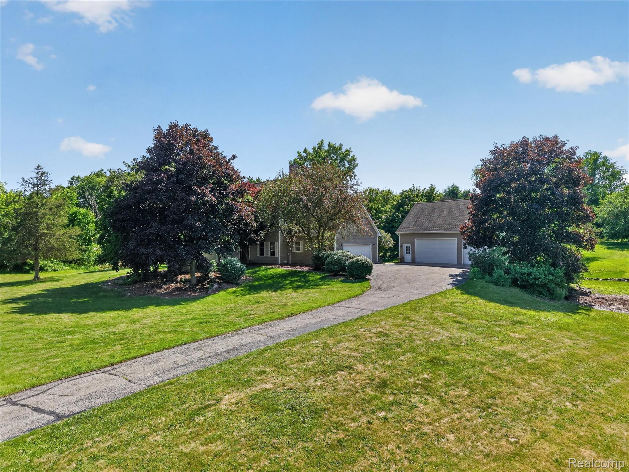 8114 Chilson Road Pinckney, MI 48169 - Photo 29 of 32 Spacious property featuring a long paved driveway, detached two-car garage, mature landscaping, and a verdant lawn