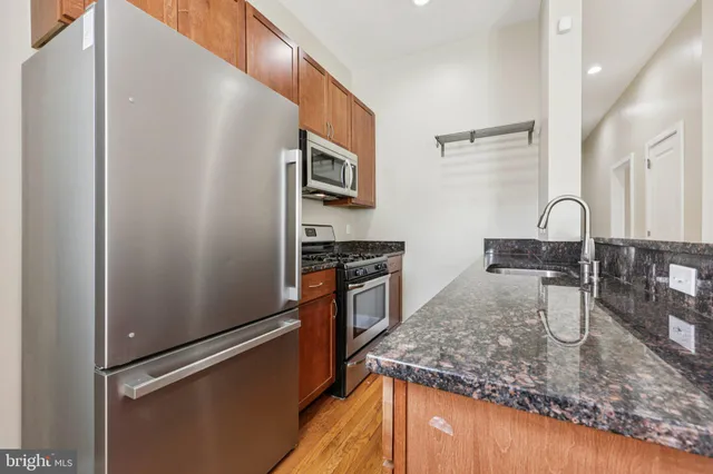 a kitchen with stainless steel appliances granite countertop a refrigerator a stove and a sink with wooden floors