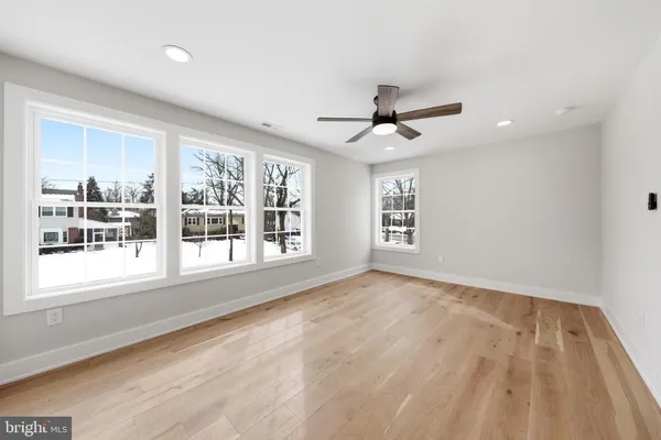 an empty room with wooden floor ceiling fan and windows