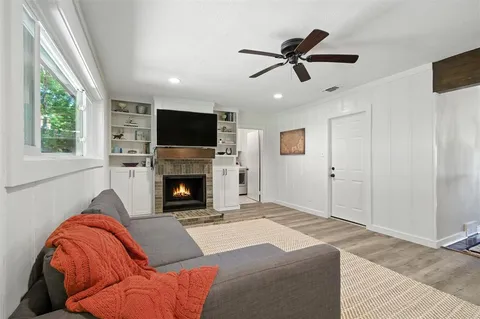 a living room with a fireplace furniture a ceiling fan and a window