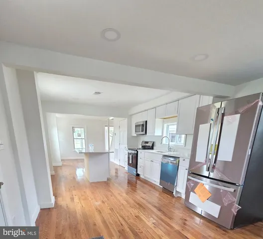 a living room with stainless steel appliances furniture a refrigerator a sink a microwave and wooden floor