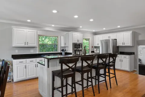 a kitchen with stainless steel appliances granite countertop white cabinets a sink a stove a dining table and chairs