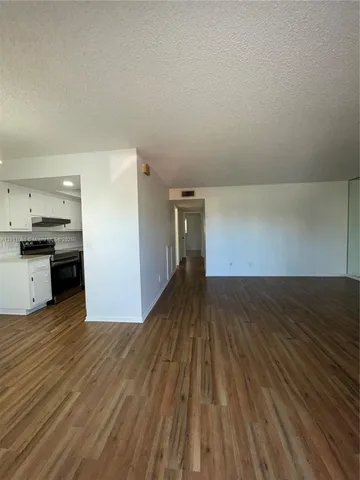 a view of kitchen and empty room with wooden floor
