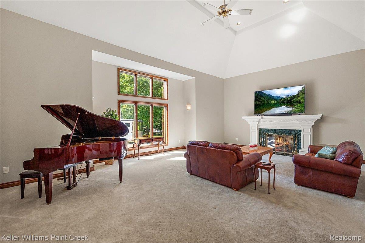 69069 Campground Road Romeo, MI 48065 - Photo 22 of 78 Spacious living area featuring a vaulted ceiling with a ceiling fan, a prominent fireplace with an ornate white mantel and green stone surround, and large multi-pane windows