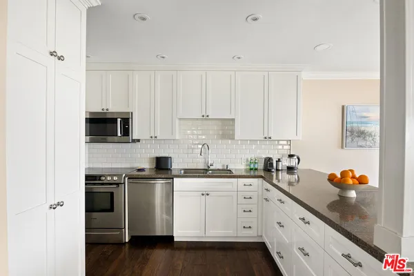 a white kitchen with stainless steel appliances granite countertop a stove a sink and white cabinets