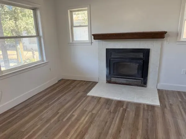an empty room with wooden floor fireplace and windows