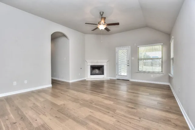 an empty room with wooden floor a ceiling fan and kitchen view