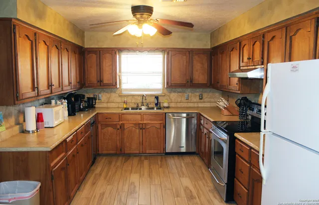 a kitchen with stainless steel appliances granite countertop a stove a sink dishwasher and a refrigerator with wooden cabinets