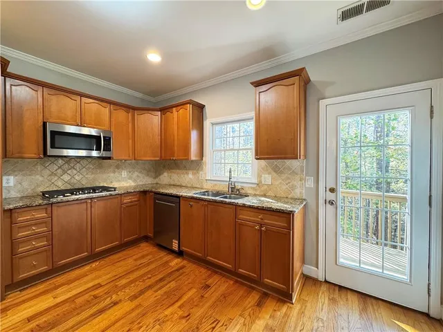 a kitchen with stainless steel appliances granite countertop wooden cabinets a stove top oven a sink and dishwasher with wooden floor