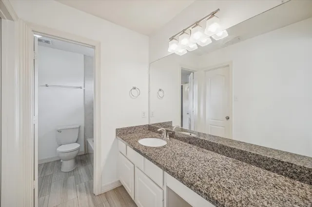 a bathroom with a granite countertop sink a toilet and a large mirror