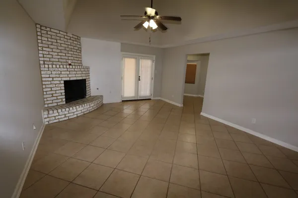 a view of an empty room with chandelier fan and fire place