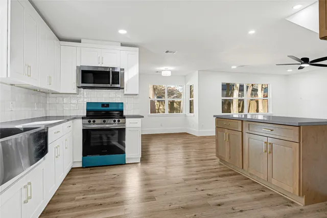 a kitchen with stainless steel appliances granite countertop a stove top oven a sink dishwasher and a refrigerator with wooden floor