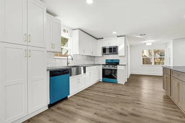 a kitchen with stainless steel appliances granite countertop a stove top oven a sink dishwasher and a refrigerator with wooden floor