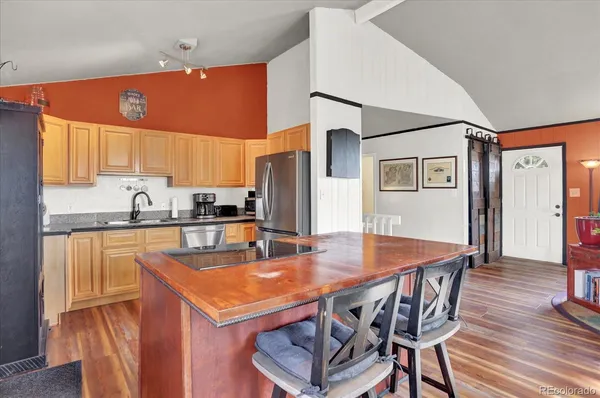 a kitchen with stainless steel appliances granite countertop a kitchen island a stove a refrigerator a sink a dining table and chairs with wooden floor