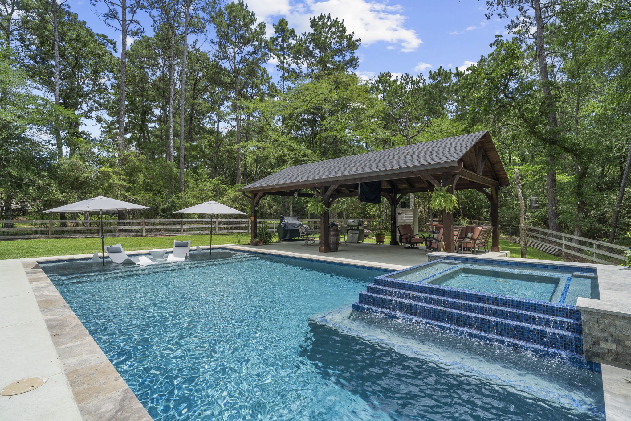 19610 Timber Ridge Drive Magnolia, TX 77355 - Photo 36 of 50 The raised spa serves as a stunning focal point, with cascading water flowing over the tiled edge into the pool below, creating both a beautiful visual feature and a soothing backdrop for outdoor relaxation.