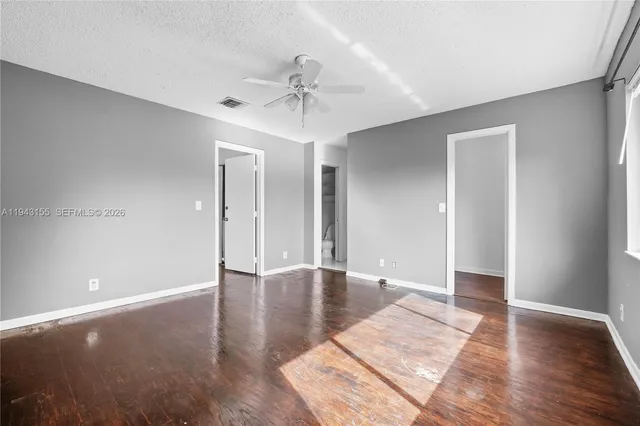 a view of an empty room with wooden floor and a ceiling fan