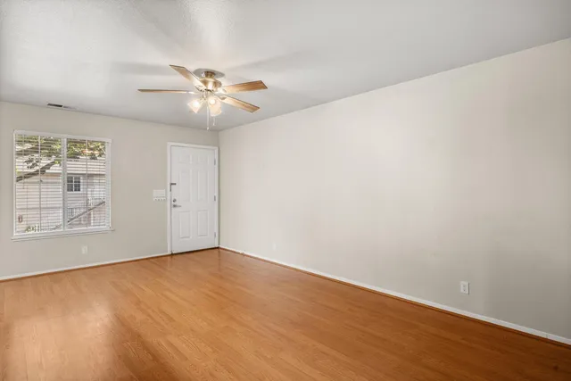 a view of an empty room with chandelier fan and wooden floor