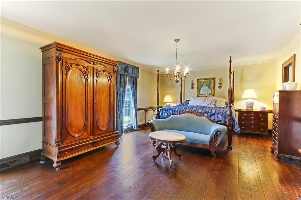1760 Simpson Road Stokesdale, NC 27357 - Photo 14 of 30 The Master Bedroom is located on the main floor. Wood flooring, chandelier, crown, base and chair moldings. Not pictured is wood burning fireplace with brick surround and wood decorative detail, and built in shelving and cabinet storage. Two large windows bring in abundant natural light. Master bath has double sinks, separate shower and tile floor.