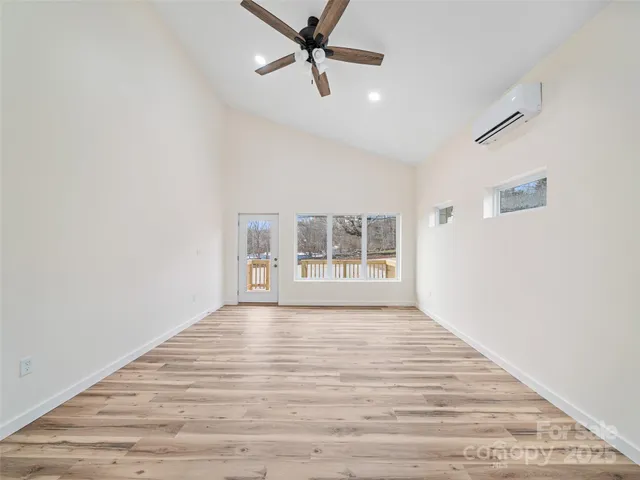an empty room with wooden floor ceiling fan and windows