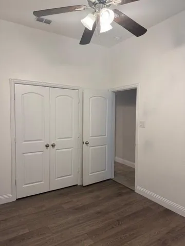 an empty room with wooden floor fan and windows