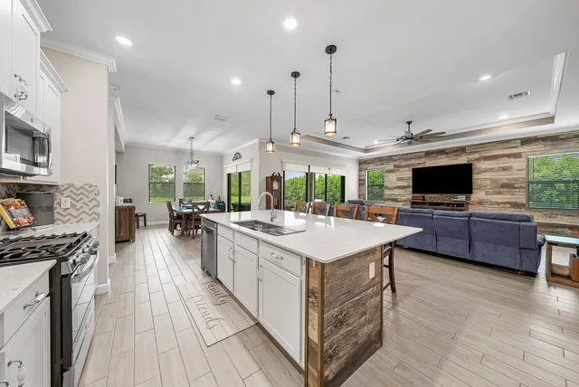 a large kitchen with stainless steel appliances a large counter top a stove a chimney a sink and a living room view