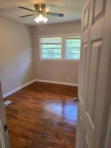 a view of empty room with wooden floor and fan
