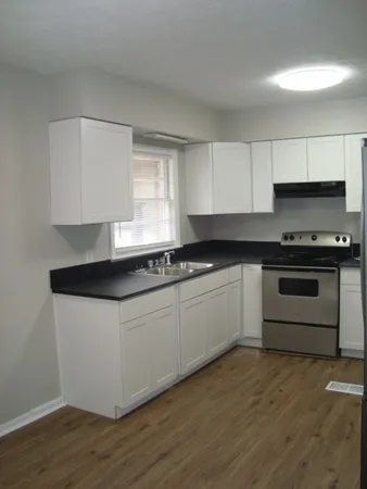 a white kitchen with granite countertop a stove a sink and a microwave