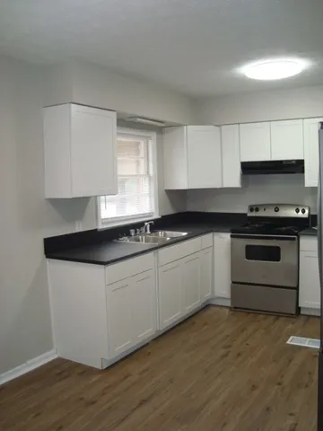 a white kitchen with granite countertop a stove a sink and a microwave