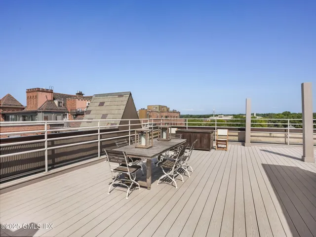 a view of a roof deck with table and chairs a barbeque with wooden floor and fence