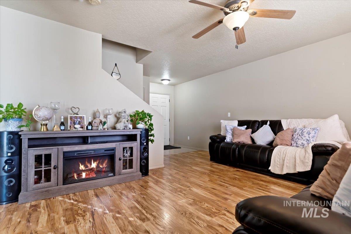 14057 Santa Cruz Street Caldwell, ID 83607 - Photo 6 of 26 Living room with a glass covered fireplace, a textured ceiling, light wood finished floors, and a ceiling fan