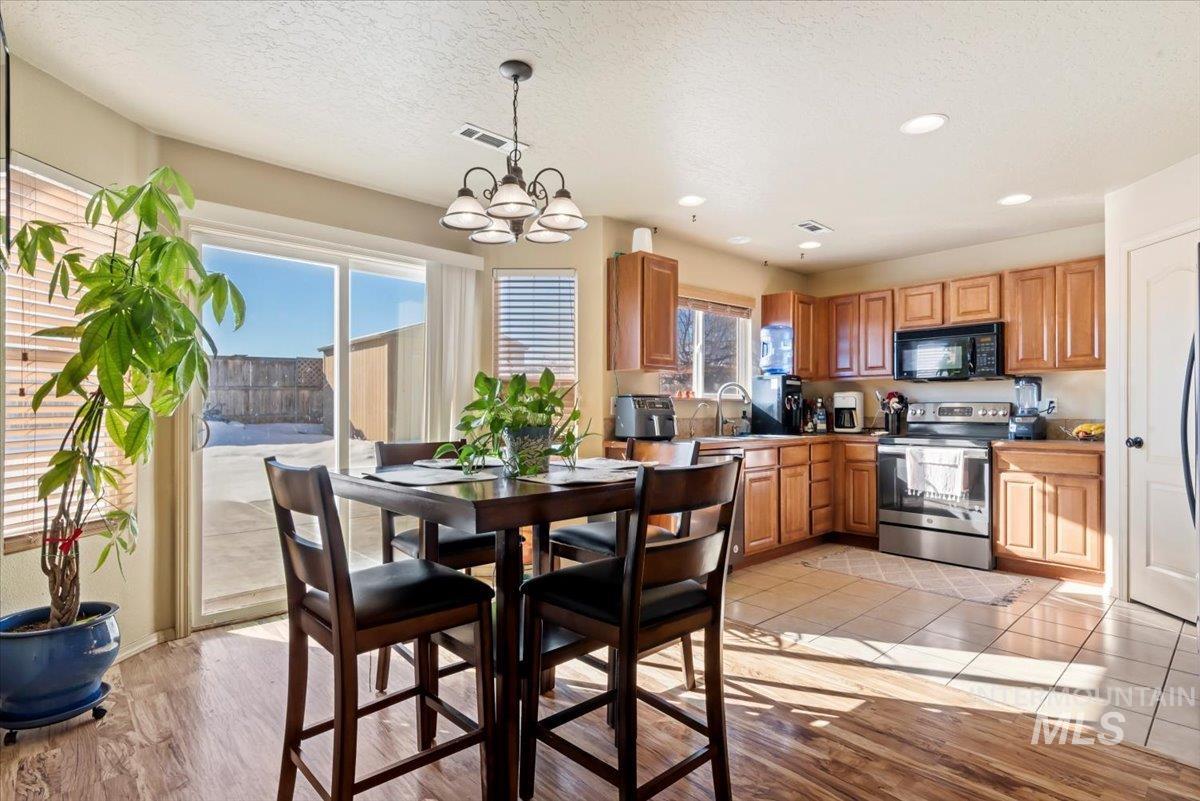 14057 Santa Cruz Street Caldwell, ID 83607 - Photo 7 of 26 Kitchen featuring stainless steel electric range oven, black microwave, hanging light fixtures, light wood-style flooring, and brown cabinets