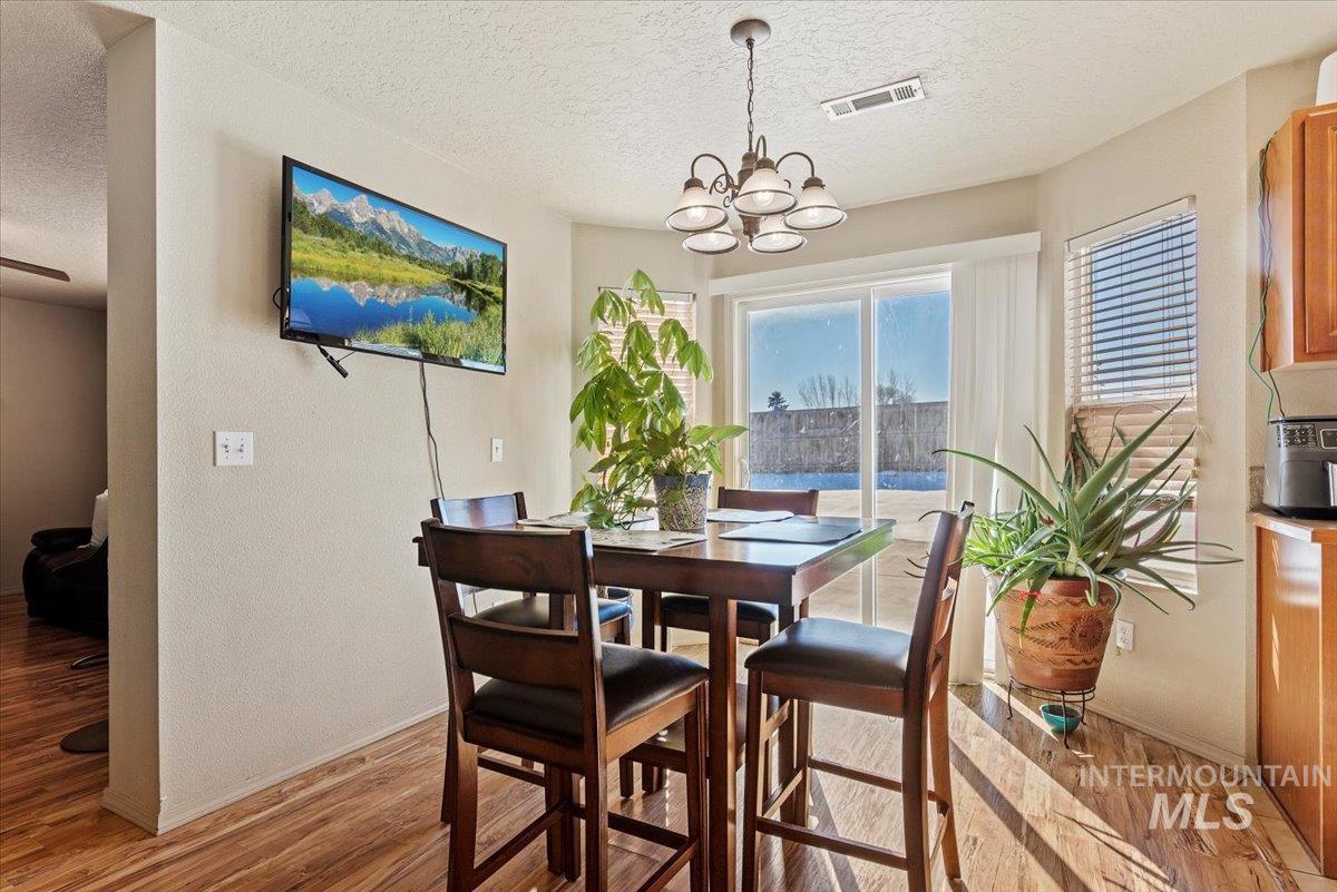 14057 Santa Cruz Street Caldwell, ID 83607 - Photo 8 of 26 Dining room with light wood-style flooring, a textured ceiling, a textured wall, and a chandelier