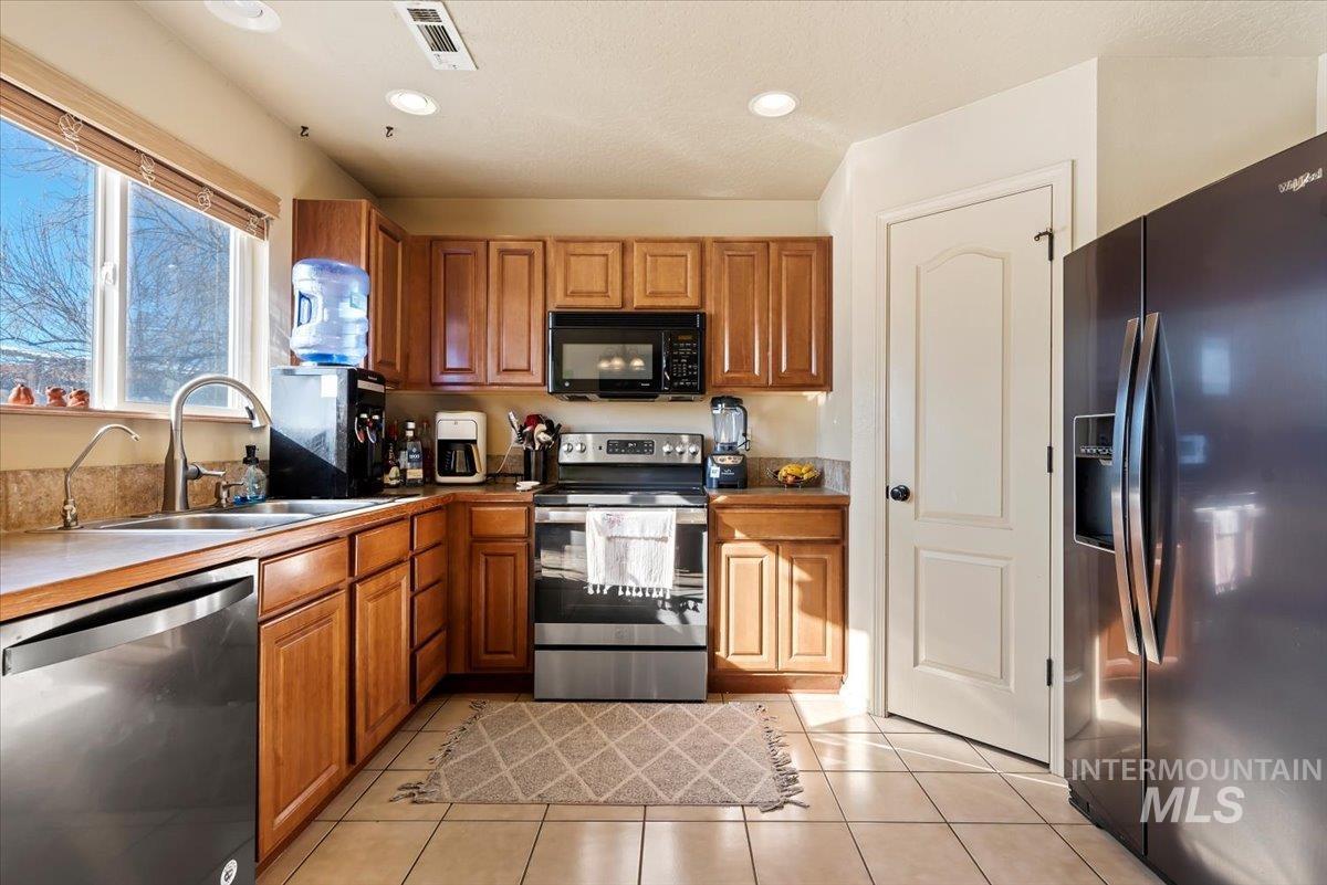 14057 Santa Cruz Street Caldwell, ID 83607 - Photo 10 of 26 Kitchen with appliances with stainless steel finishes, brown cabinets, light tile patterned floors, recessed lighting, and dark countertops