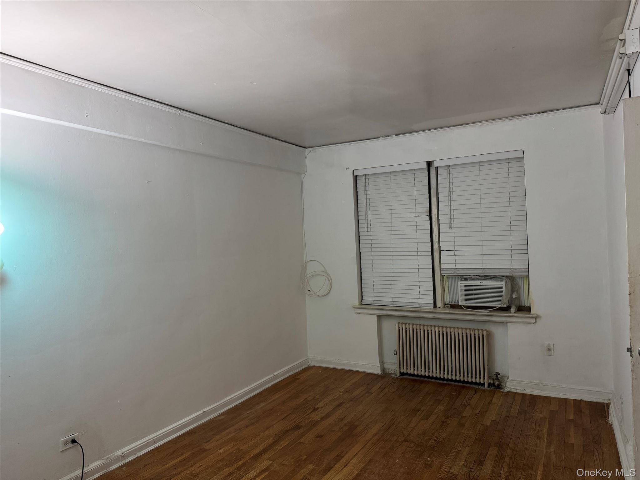 141-17 78th Road, Unit 1O Queens, NY 11367 - Photo 8 of 17 Spare room with dark wood-type flooring, radiator, and cooling unit