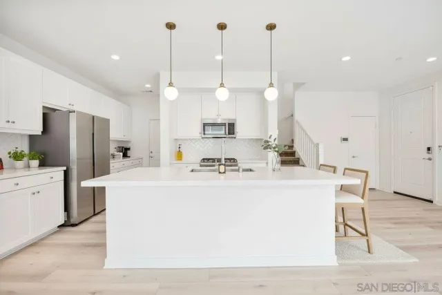a large white kitchen with a refrigerator a sink and a wooden floor