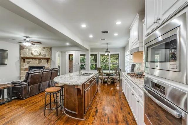 a kitchen with stainless steel appliances granite countertop a stove top oven a sink dishwasher a dining table and chairs with wooden floor