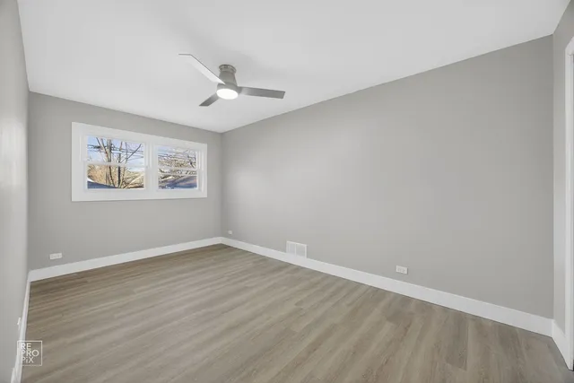 an empty room with wooden floor ceiling fan and windows