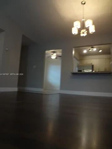 an empty room with wooden floor chandelier and windows