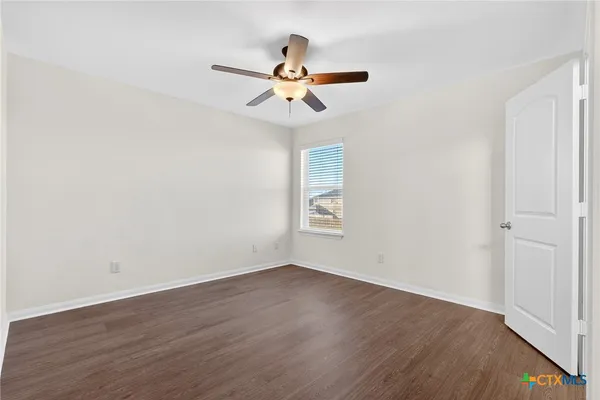 an empty room with wooden floor ceiling fan and window