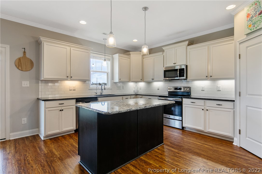 5213 Bree Bridge Road Hope Mills, NC 28348 - Photo 19 of 50 a kitchen with kitchen island granite countertop a sink cabinets and wooden floor
