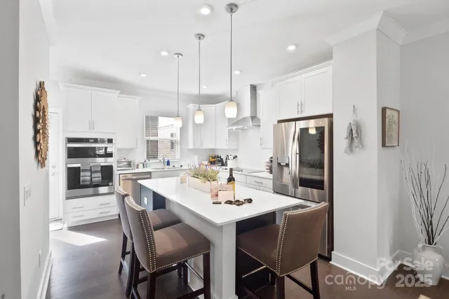 a kitchen with stainless steel appliances kitchen island granite countertop a dining table chairs and a refrigerator