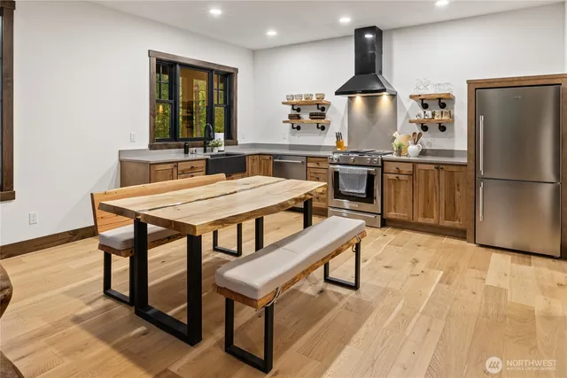a kitchen with stainless steel appliances kitchen island granite countertop a refrigerator a stove a sink a dining table and chairs with wooden floor
