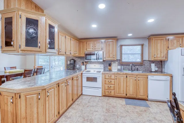 a kitchen with stainless steel appliances granite countertop a stove top oven a sink dishwasher and a refrigerator with wooden cabinets