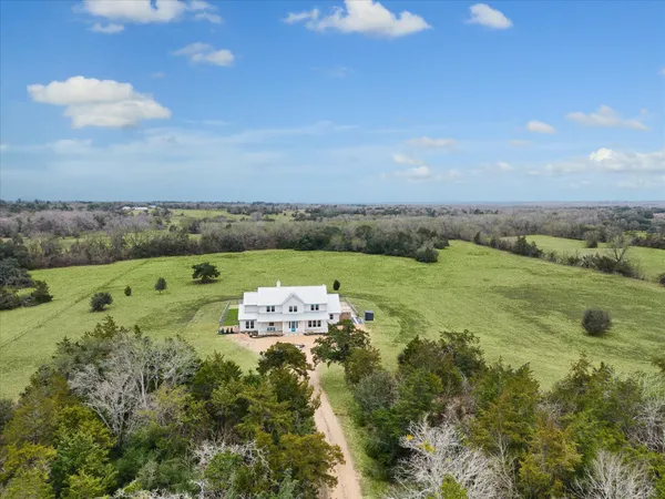 an aerial view of a houses with outdoor space and trees all around